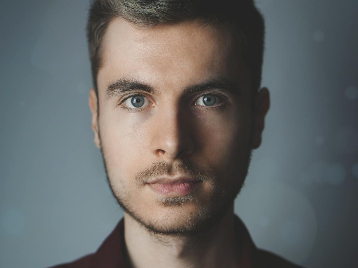 Close-up portrait of a young man with facial hair and a serious expression.