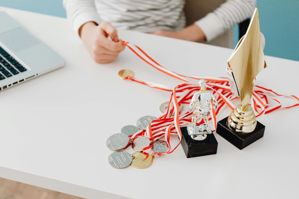 Young person displays football trophies and medals on a desk, showcasing athletic pride.