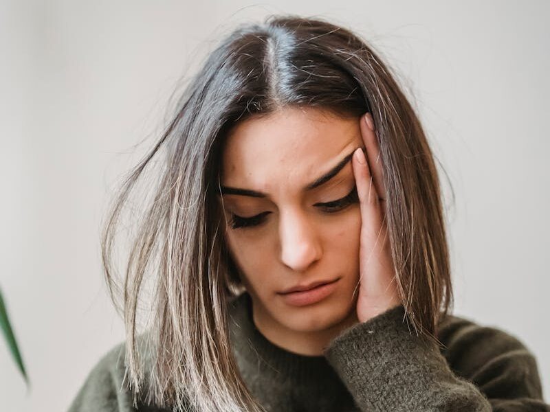 Unhappy female in casual wear leaning on hand and surfing internet on cellphone while sitting in light room near wall at home