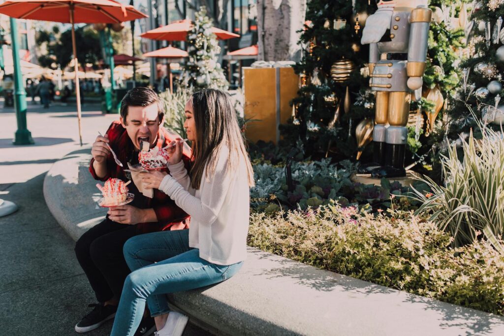 Couple enjoys ice cream on a sunny day in a festive outdoor setting with holiday decor.