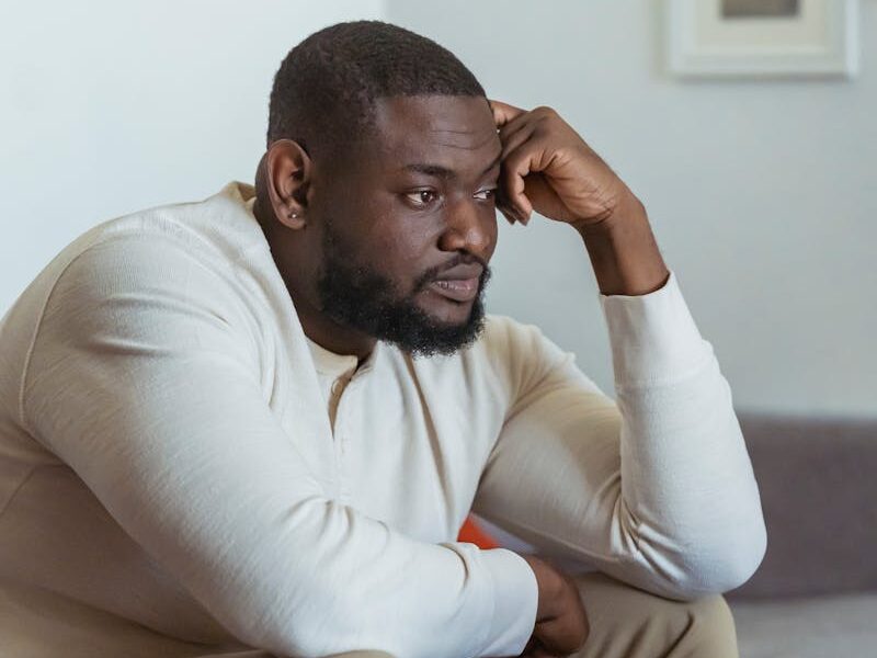 A thoughtful adult man sits in a cozy home setting, focused on his laptop.