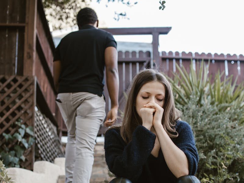 A woman sitting in distress while a man walks away outdoors, capturing emotion and separation.