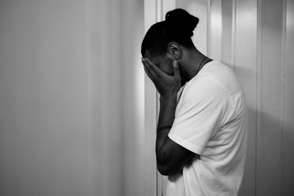 Black and white portrait of a man exhibiting stress, touching his face in an indoor setting.