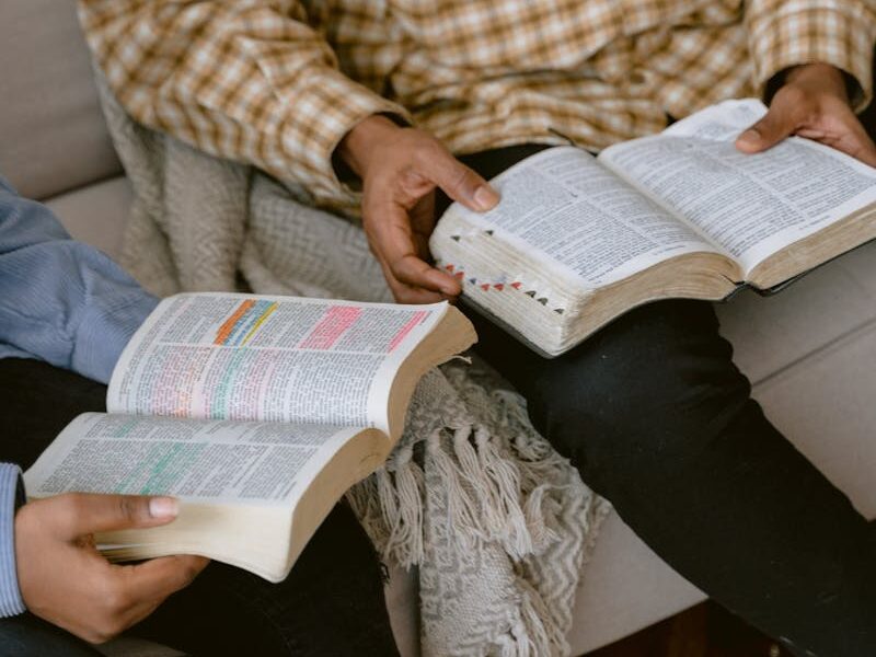 Two individuals sitting on a sofa reading and discussing the Bible indoors.