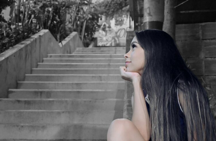 Woman gazes thoughtfully next to stairs.