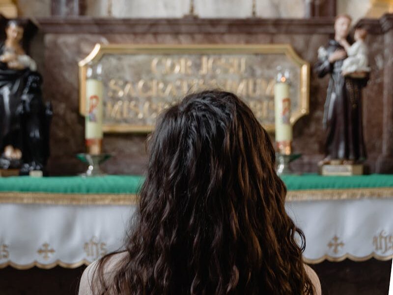 A woman in deep prayer before an altar featuring the Sacred Heart of Jesus in a church.