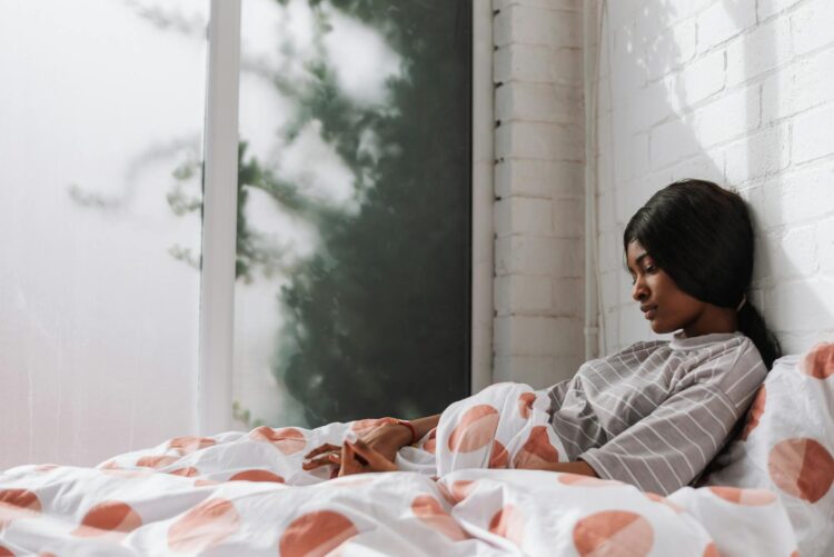 A thoughtful teenager sits on a bed near a window, holding a coffee cup, in a calm indoor setting.