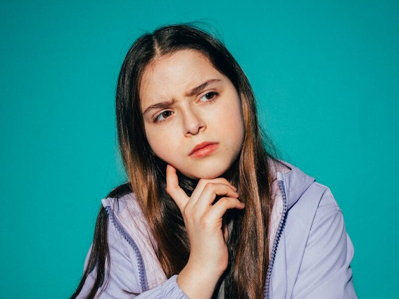A young girl pondering deeply against a vibrant teal background.
