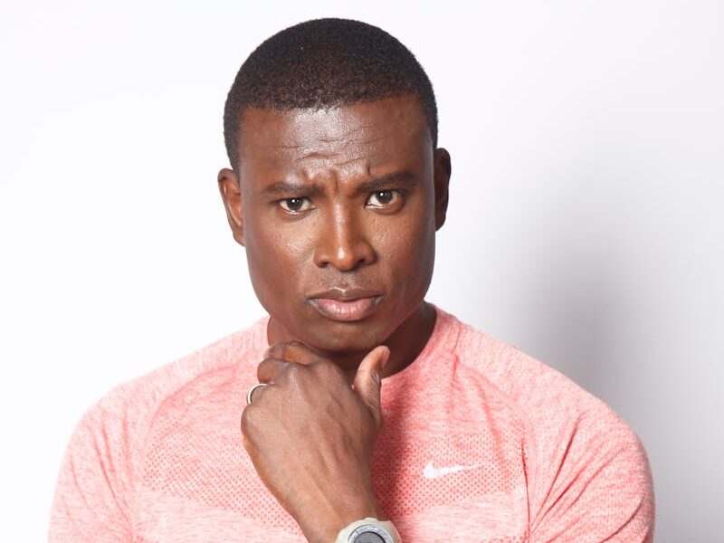 Athletic black man in a pink sports shirt poses with a pensive expression, showcasing fitness and style.