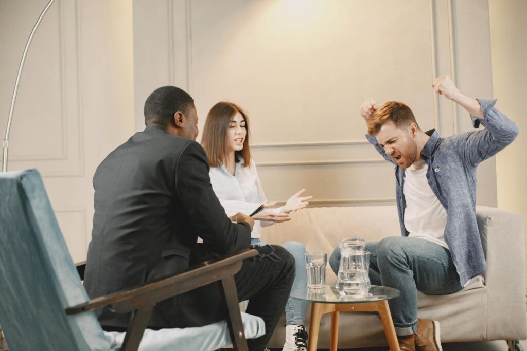 A couple engaging in a heated discussion during a therapy session with a therapist.