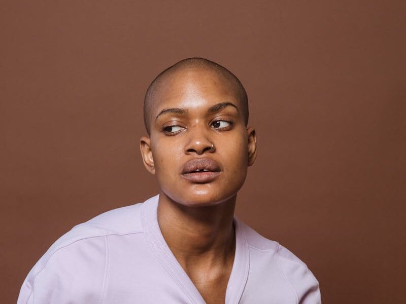 African American model with shaved head looking away while touching pink long sleeve shirt on brown background