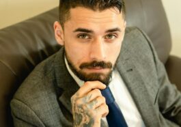 Portrait of a bearded businessman with formal attire sitting confidently indoors.