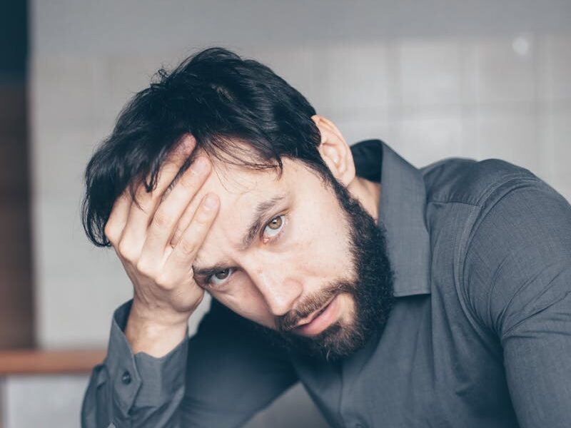 Thoughtful man sitting at a table with glasses and cup, showing frustration.