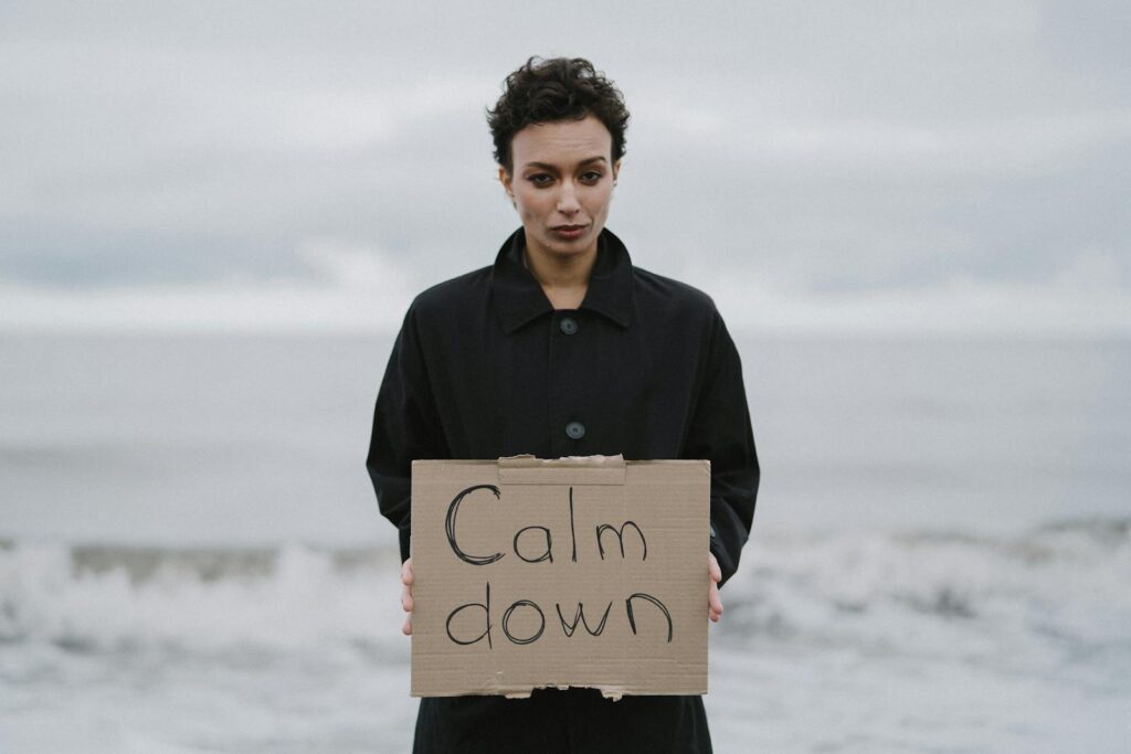 Individual holding 'Calm Down' sign at the beach on a cloudy day.