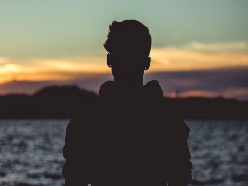 A silhouetted man stands by Lake Ozark during a beautiful sunset, creating a peaceful and serene scene.