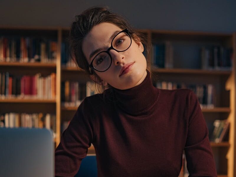 A woman in glasses studies intently at a library work desk, surrounded by books.