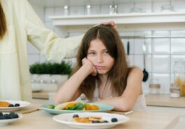 Young girl looking displeased with breakfast in a home kitchen setting.