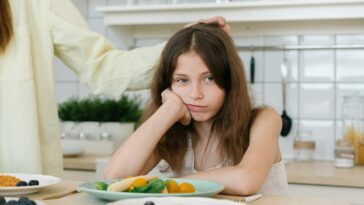 Young girl looking displeased with breakfast in a home kitchen setting.