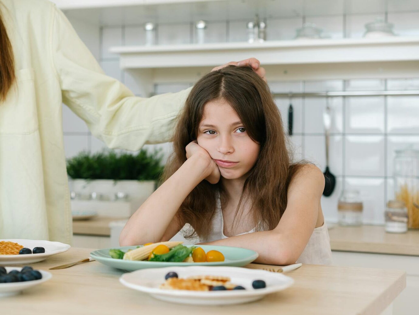 Young girl looking displeased with breakfast in a home kitchen setting.