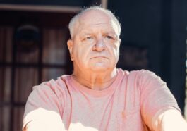 A senior man with a thoughtful expression, sitting outdoors in sunlight.