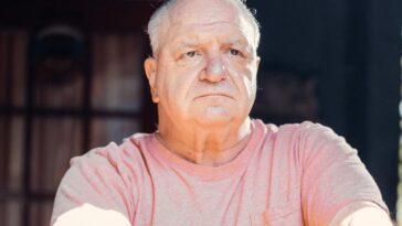 A senior man with a thoughtful expression, sitting outdoors in sunlight.