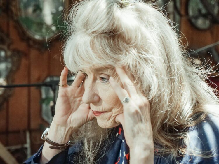 A thoughtful elderly woman in a close-up portrait with hands on face.