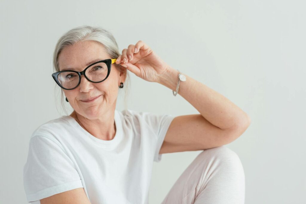 A happy senior woman wearing stylish eyeglasses poses indoors with a warm smile.