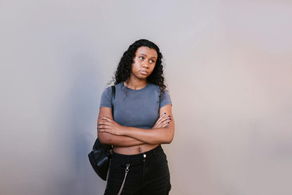 Teen girl standing with arms crossed and looking sideways. Neutral background offering negative space.