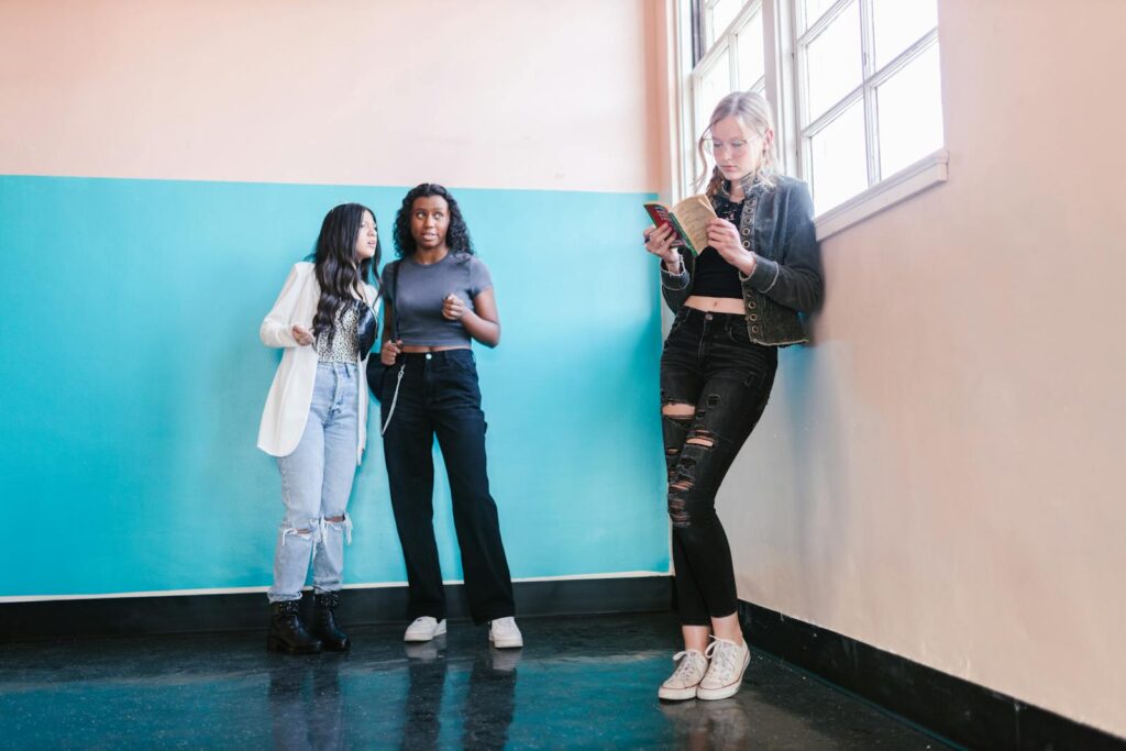 Group of teenagers in a hallway, two talking, one reading a book.