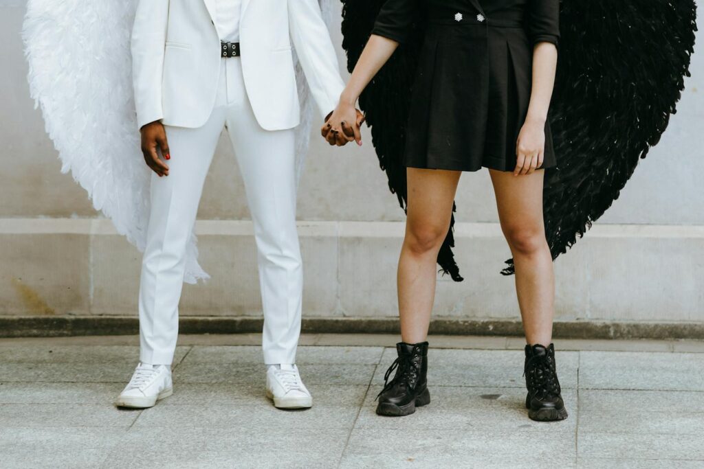 A couple dressed as angels in black and white attire holding hands in an urban setting.