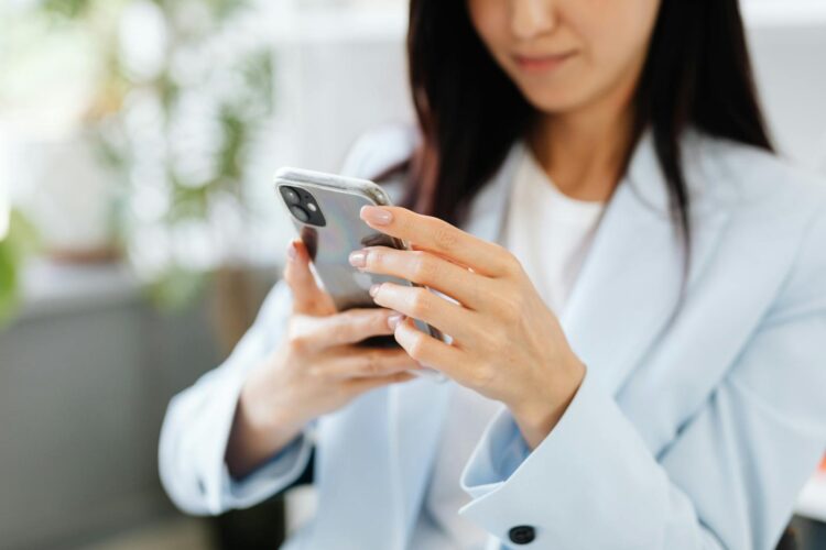 A woman with manicured nails uses a smartphone inside a modern setting.