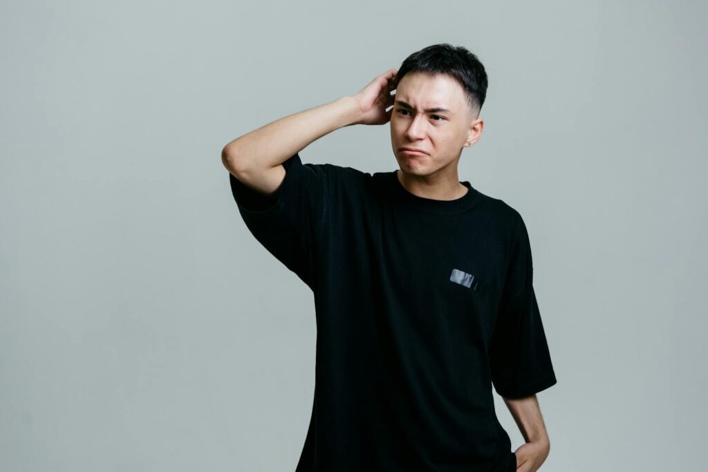 Studio portrait of a young man looking puzzled against a gray background.