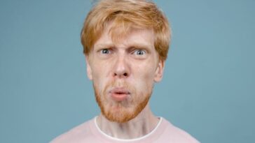 Adult man with angry facial expression in pink shirt, studio shot with blue background.