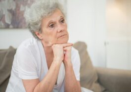 A thoughtful senior woman with gray hair sitting indoors, reflecting.