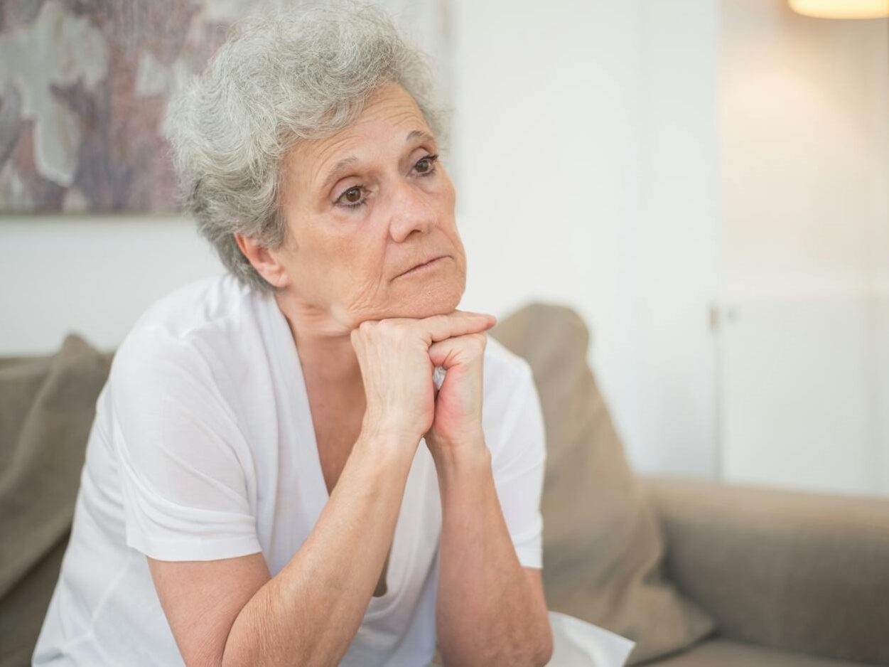 A thoughtful senior woman with gray hair sitting indoors, reflecting.