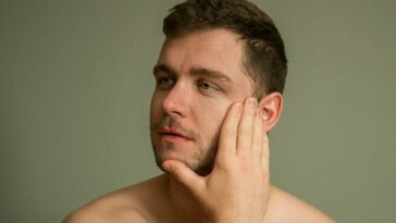 topless man covering his face with his hand