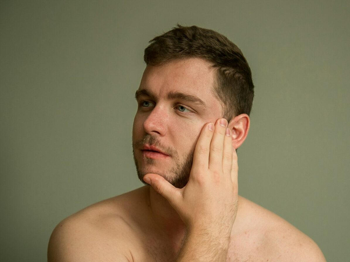 topless man covering his face with his hand