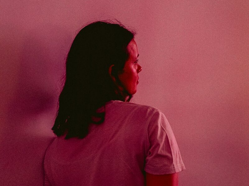 a woman sitting on a stool in front of a pink wall