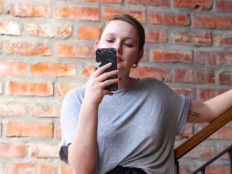 woman in gray crew neck t-shirt and black skirt holding black smartphone