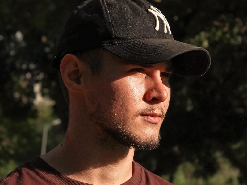 a man wearing a hat standing in front of a tree
