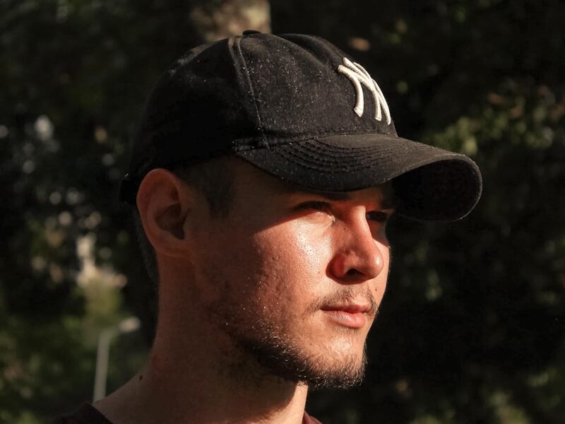 a man wearing a hat standing in front of a tree