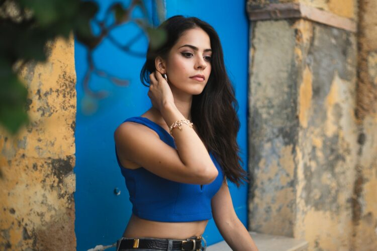 woman in blue tank top and blue denim shorts leaning on brown concrete wall during daytime