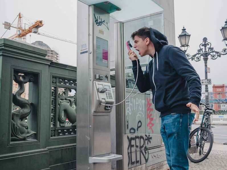 man in black jacket and blue denim jeans standing near black telephone booth during daytime
