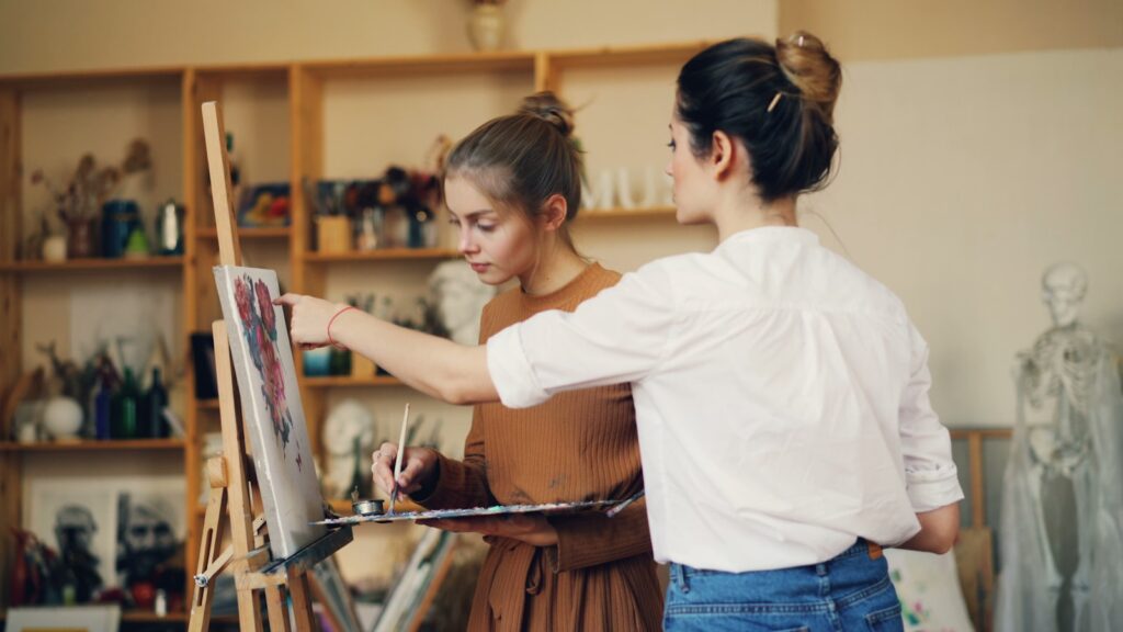 Two women collaborate on a painting in an art studio.
