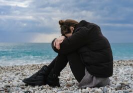 a woman sitting on a rocky beach with her head in her hands