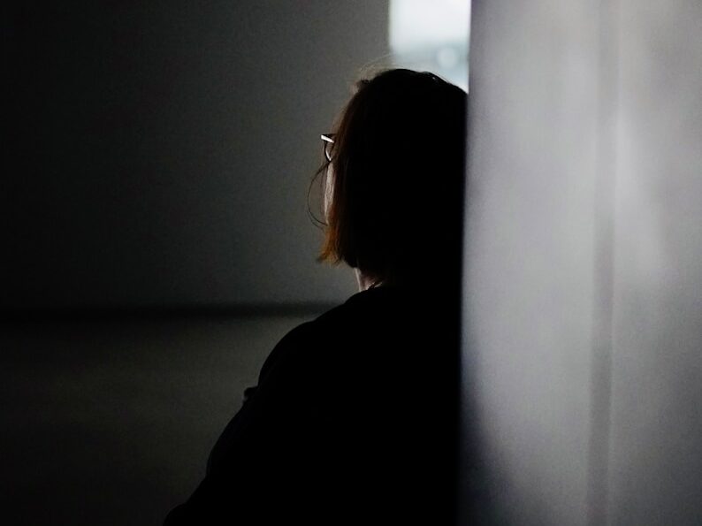 a woman sitting in a dark room next to a wall