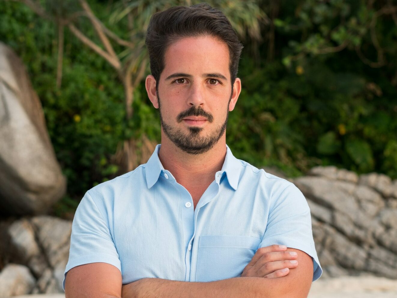 A man standing with his arms crossed on a beach