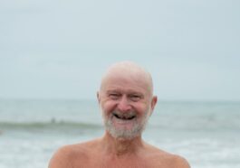 an older man standing on the beach with his arms crossed