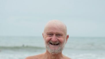 an older man standing on the beach with his arms crossed