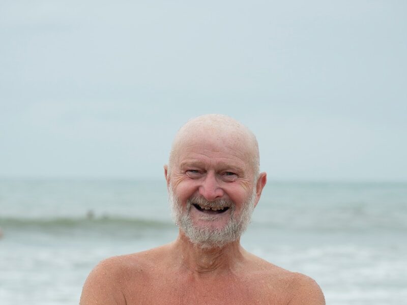 an older man standing on the beach with his arms crossed